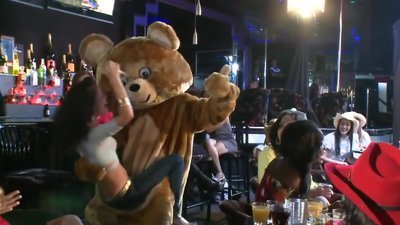 Stripper dressed like teddy bear climbs on stage and starts having fun around club. He is joined by athletic colleague who finds lucky MILF and brings